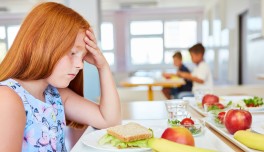 Nena trista davant d'un plat en un menjador escolar