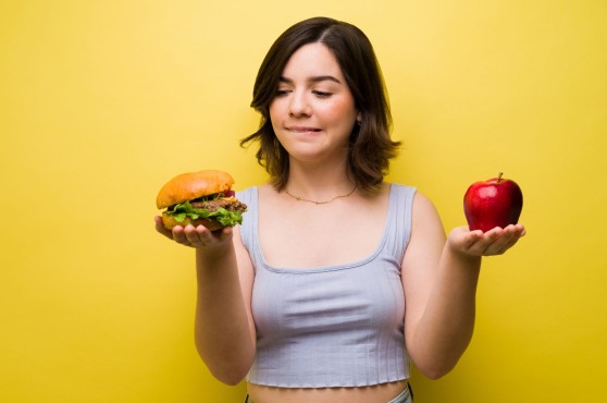 Chica dudando entre comer hamburguesa o manzana.